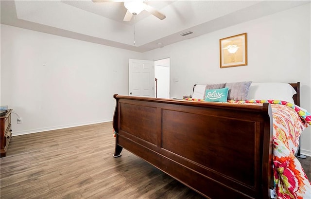 bedroom with hardwood / wood-style flooring, a raised ceiling, and ceiling fan