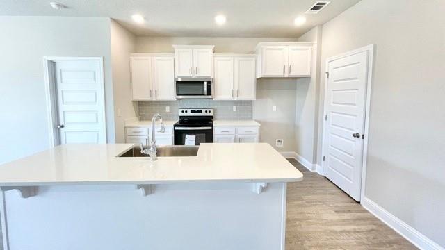 kitchen featuring a kitchen bar, sink, an island with sink, electric stove, and white cabinets