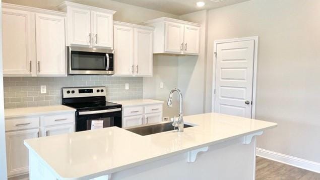 kitchen featuring sink, white cabinetry, electric range, an island with sink, and decorative backsplash