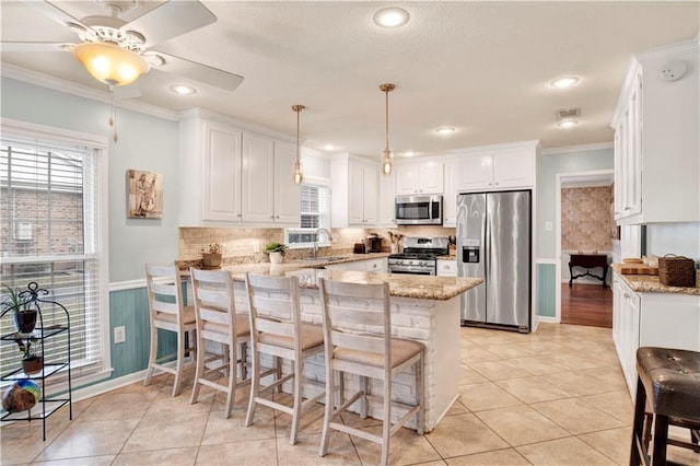 kitchen with hanging light fixtures, ornamental molding, white cabinetry, kitchen peninsula, and stainless steel appliances