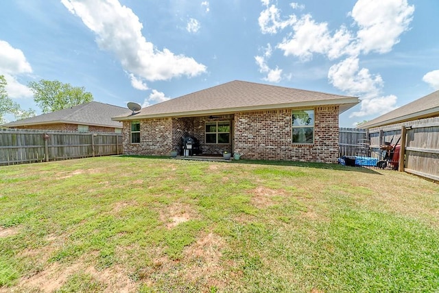 rear view of house featuring brick siding, a fenced backyard, and a yard