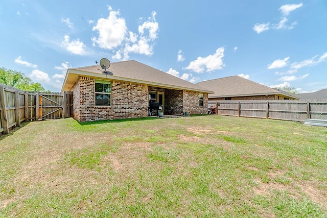 back of house with brick siding, a fenced backyard, and a yard