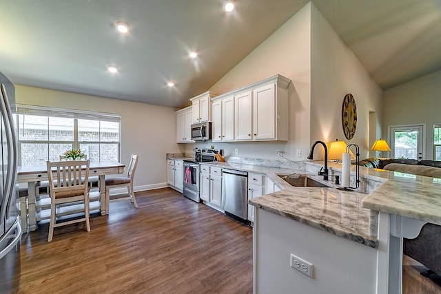 kitchen with white cabinets, dark wood-style flooring, a sink, stainless steel appliances, and a peninsula