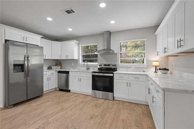 kitchen featuring light wood-type flooring, stainless steel appliances, a sink, visible vents, and wall chimney range hood