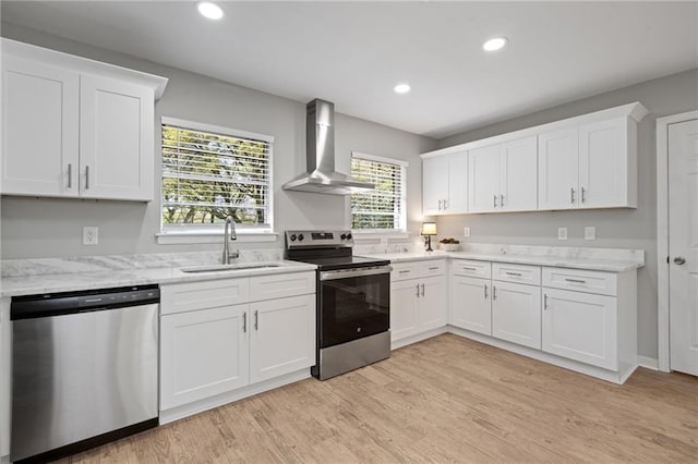 kitchen with wall chimney range hood, white cabinets, a sink, and stainless steel appliances