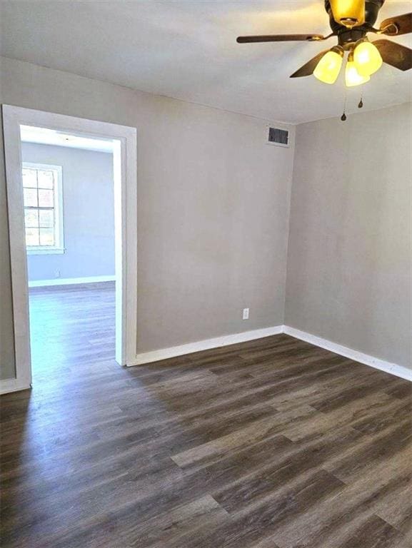 spare room with a ceiling fan, visible vents, dark wood finished floors, and baseboards