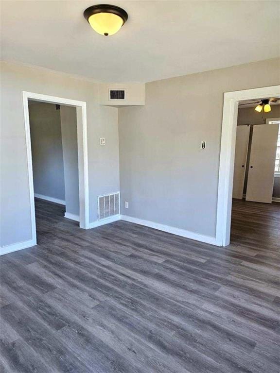 unfurnished room featuring dark wood-type flooring, visible vents, and baseboards