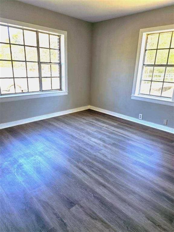 unfurnished room featuring plenty of natural light, dark wood finished floors, and baseboards