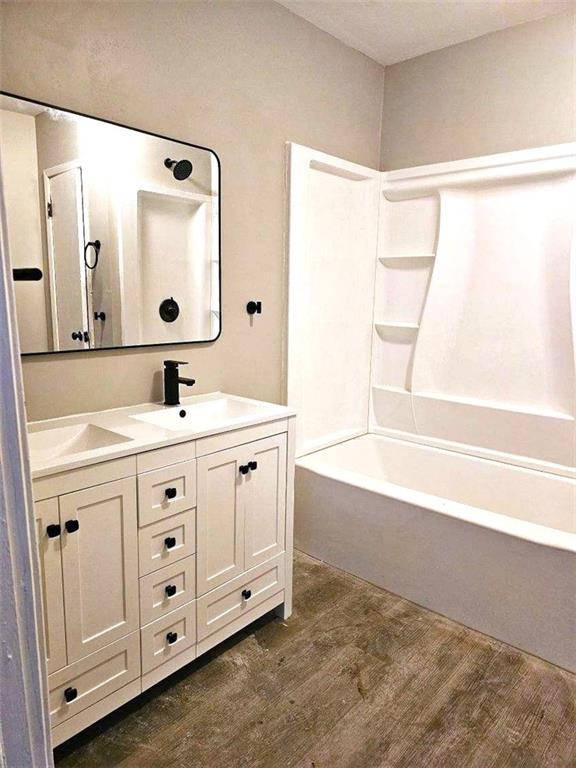 full bathroom featuring double vanity, wood finished floors, a sink, and shower / bathing tub combination