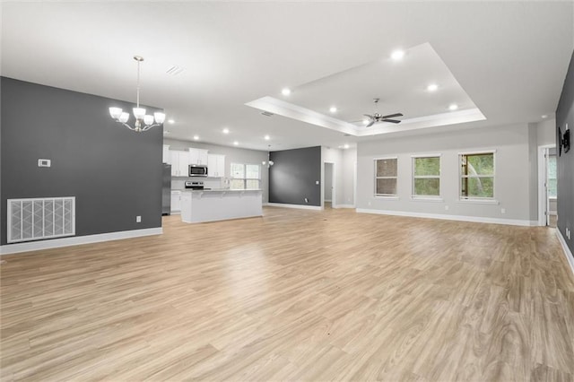 unfurnished living room with ceiling fan with notable chandelier, light hardwood / wood-style floors, and a raised ceiling