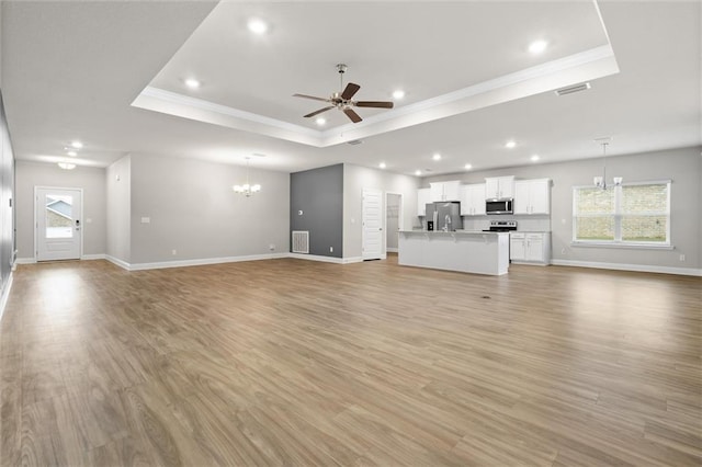 unfurnished living room featuring ceiling fan with notable chandelier, light wood-type flooring, a raised ceiling, and crown molding