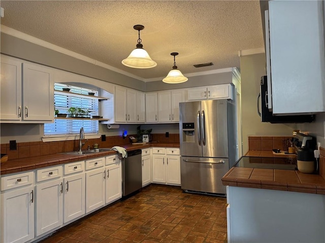 kitchen with a sink, brick floor, tile counters, stainless steel appliances, and white cabinetry
