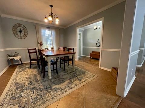 tiled dining room featuring baseboards, ornamental molding, and a chandelier