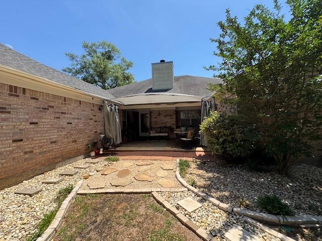 rear view of house with brick siding, a patio, and a chimney