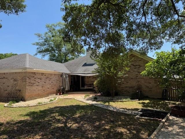 exterior space featuring roof with shingles, a yard, and brick siding