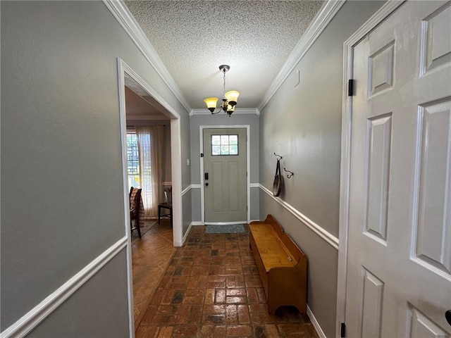 entryway featuring a textured ceiling, crown molding, baseboards, an inviting chandelier, and brick floor
