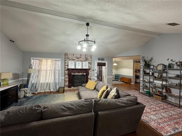 living room with an inviting chandelier, a brick fireplace, a textured ceiling, and wood finished floors