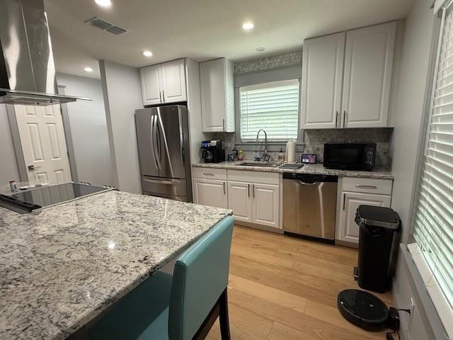 1071 Coke Ct, Mobile, AL 36695 - kitchen featuring appliances with stainless steel finishes, island range hood, white cabinetry, light wood-style floors, and decorative backsplash