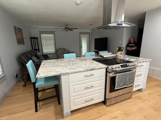 1071 Coke Ct, Mobile, AL 36695 - kitchen with wall chimney exhaust hood, stainless steel range with electric stovetop, open floor plan, ceiling fan, and light wood finished floors