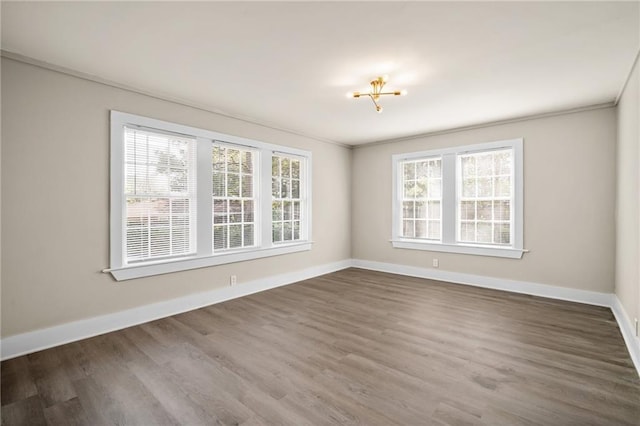 spare room with wood-type flooring, ornamental molding, and an inviting chandelier