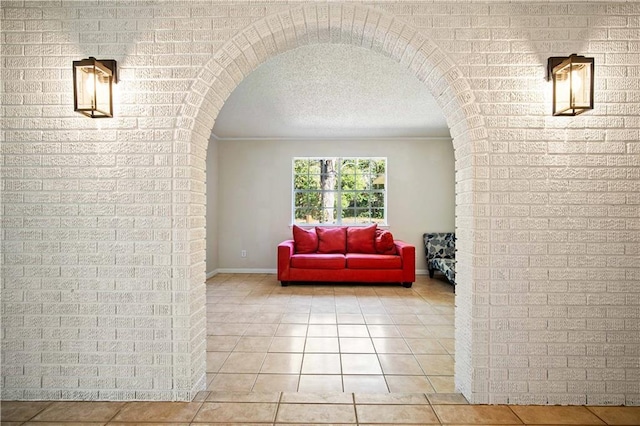 hall with light tile patterned floors, a textured ceiling, and brick wall