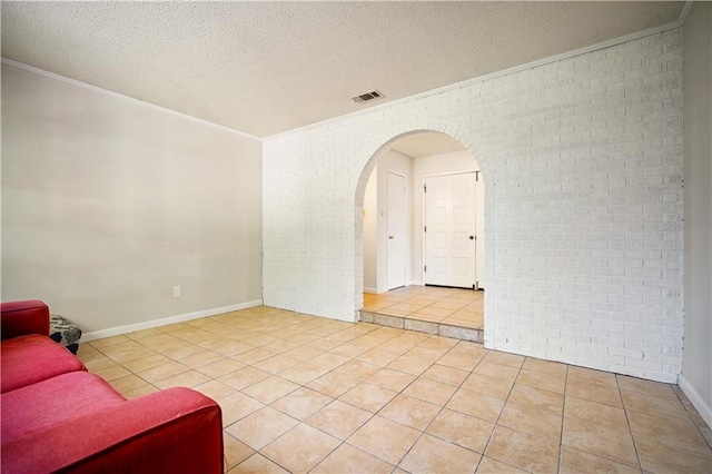 tiled empty room with ornamental molding, brick wall, and a textured ceiling