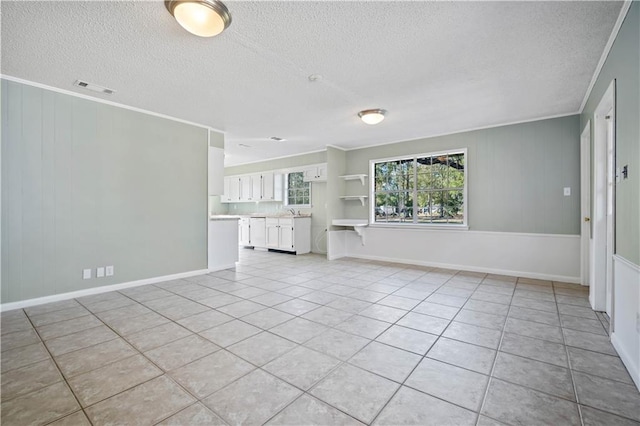 unfurnished living room with light tile patterned flooring, sink, a textured ceiling, and crown molding