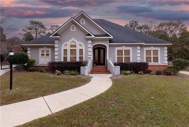 view of front facade featuring a shingled roof, stucco siding, french doors, a lawn, and brick siding