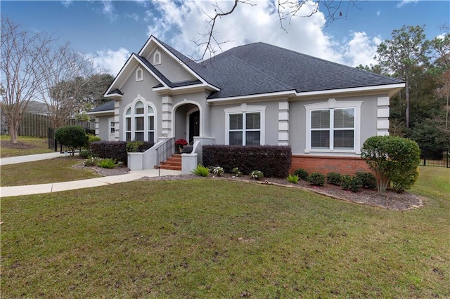 view of front of property with stucco siding, a front lawn, fence, a shingled roof, and brick siding