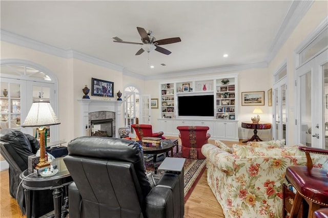 living area with crown molding, ceiling fan, light wood-type flooring, a tile fireplace, and french doors