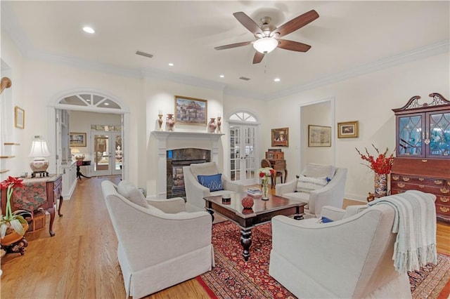 living room featuring light wood finished floors, french doors, crown molding, a fireplace, and baseboards