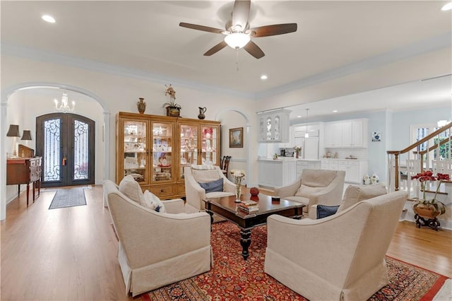 living area with light wood-style floors, french doors, arched walkways, and ornamental molding