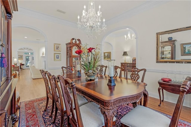 dining space with visible vents, ornamental molding, wood finished floors, arched walkways, and a chandelier