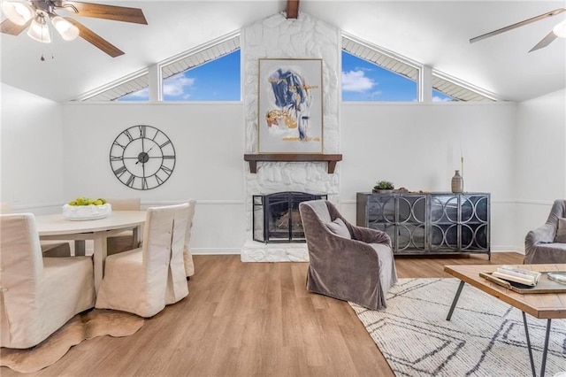 living area featuring vaulted ceiling with beams, baseboards, ceiling fan, a stone fireplace, and wood finished floors