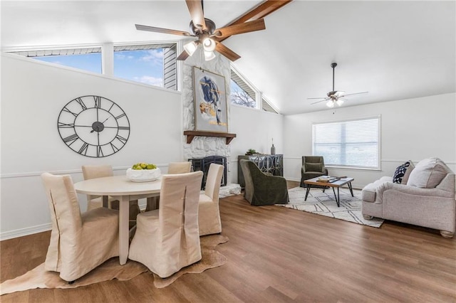 dining space with wood finished floors, baseboards, high vaulted ceiling, a fireplace, and ceiling fan