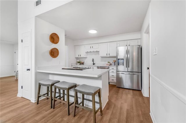 kitchen with wood finished floors, visible vents, white cabinetry, stainless steel fridge, and a kitchen bar