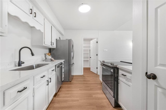 kitchen featuring light stone countertops, a sink, stainless steel appliances, white cabinetry, and light wood-type flooring