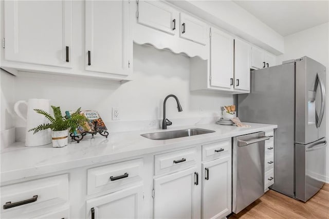 kitchen featuring light stone counters, a sink, appliances with stainless steel finishes, white cabinetry, and light wood-type flooring