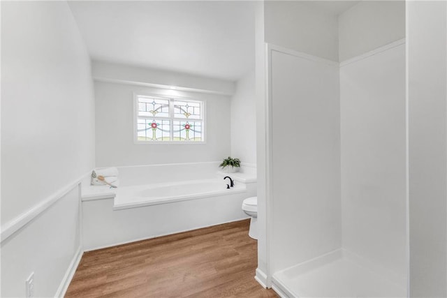 bathroom with toilet, a garden tub, and wood finished floors