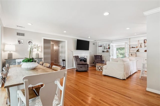 living room with crown molding, built in features, and light wood-type flooring