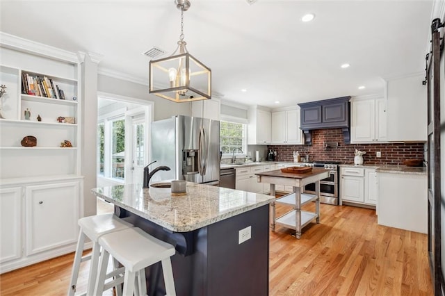 kitchen with light stone counters, decorative light fixtures, a kitchen island, stainless steel appliances, and white cabinets