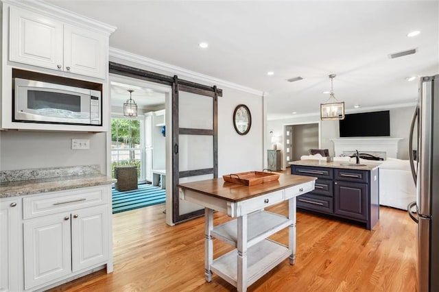 kitchen with appliances with stainless steel finishes, white cabinetry, light stone counters, ornamental molding, and a barn door