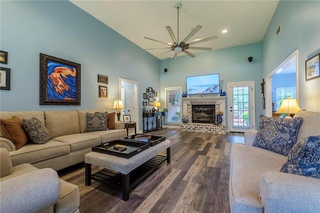 living room featuring hardwood / wood-style flooring, high vaulted ceiling, a brick fireplace, and ceiling fan