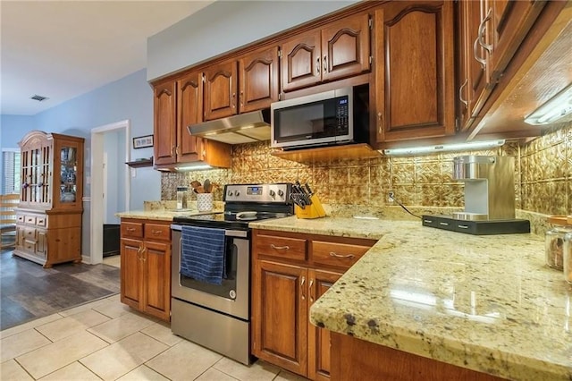 kitchen with appliances with stainless steel finishes, light hardwood / wood-style flooring, decorative backsplash, and light stone countertops