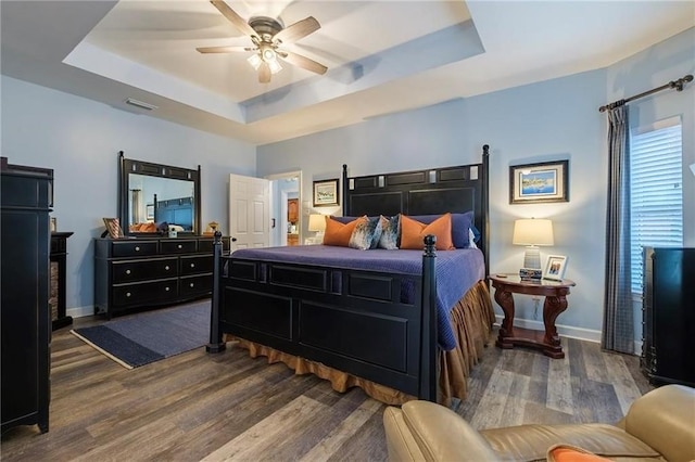 bedroom featuring dark wood-type flooring, a tray ceiling, and ceiling fan