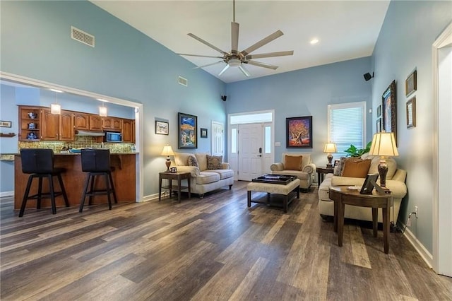 living room featuring dark wood-type flooring, ceiling fan, and a towering ceiling