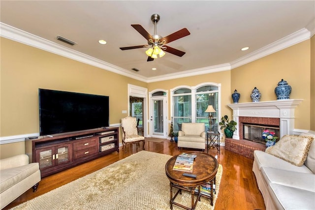 living room featuring a brick fireplace, hardwood / wood-style flooring, ceiling fan, and ornamental molding