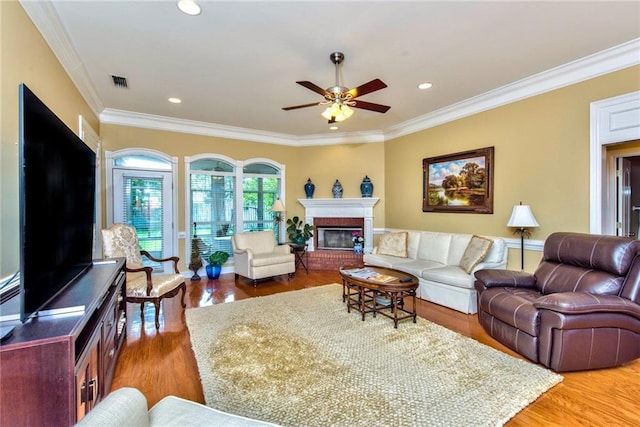 living room with ceiling fan, wood-type flooring, ornamental molding, and a brick fireplace