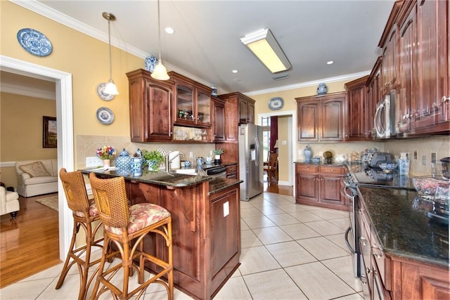 kitchen featuring crown molding, appliances with stainless steel finishes, decorative light fixtures, light tile patterned flooring, and a breakfast bar area