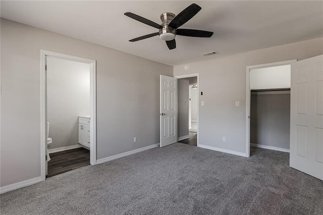 unfurnished bedroom featuring dark carpet, ensuite bath, a closet, and ceiling fan